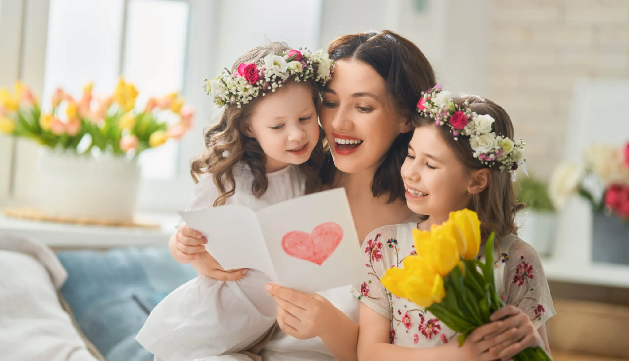 A mother with her daughters opening a mother's day card with a heart on the front.