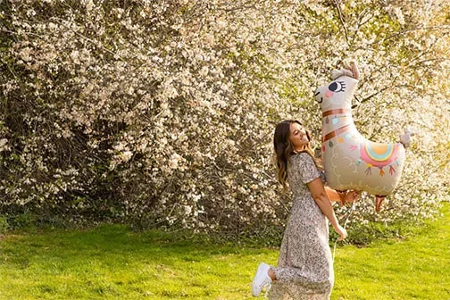 Woman holding a unicorn balloon in front of a blossom tree